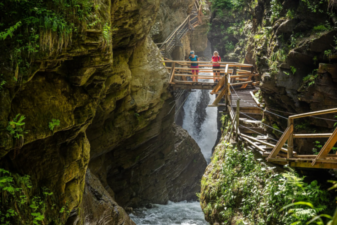 Wanderer auf Holzsteg in einer Schlucht mit Wasserfall